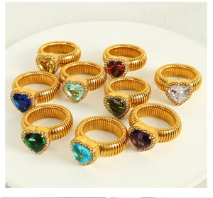 Macro view of ten colorful heart-shaped crystal rings on a white tray with golden bands