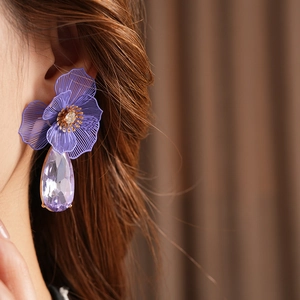 Close-up of elegant flower stud earring with purple teardrop crystal pendant on model