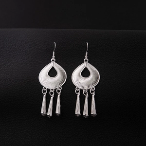 Close-up of ethnic silver-style teardrop earrings with leaf tassel on black leather