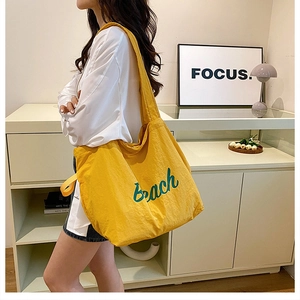 Close-up of yellow drawstring canvas tote with Beach embroidery shown on model
