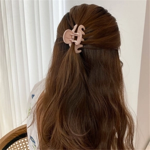 Detalle de una pinza para el cabello rosa claro mate en pelo largo ondulado