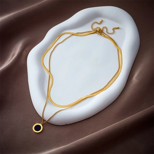 Double-layer gold snake chain necklace with black Roman pendant on white tray and silk