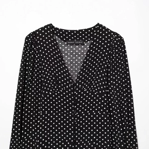 Elegante abito nero a maniche lunghe con scollo a V e motivo a pois bianchi su sfondo bianco