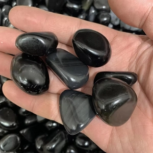 Polished black obsidian tumbled stones for fish tank decor held in a hand for size comparison