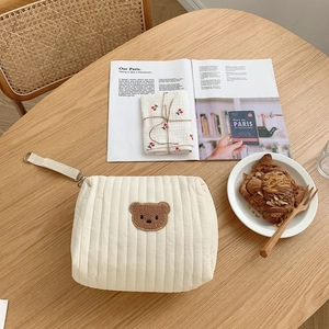 Quilted off-white storage bag featuring brown bear embroidery and webbing strap