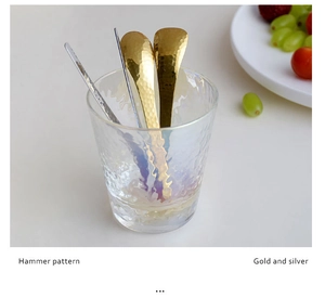 Detail of hammer pattern dessert spoons in gold and silver finish inside a glass cup