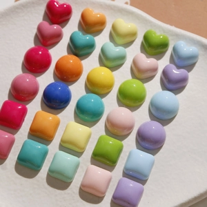 Colorful heart and round resin DIY craft beads on a white ceramic plate