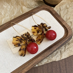 Close-up of vintage leopard acrylic flower earrings with red pearls on a wooden tray