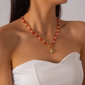 Detail of beaded necklace with red and white beads and a golden maple leaf pendant