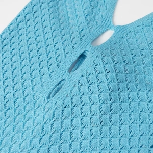 Vue macro du tissu en maille bleue avec motifs ajourés et détail de la bride du bouton
