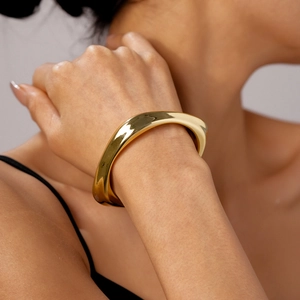 Detail of a wavy irregular gold bangle featuring a high-polish metallic mirror finish
