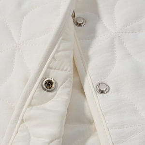 Close-up of white quilted jacket featuring metallic snap buttons and floral stitching