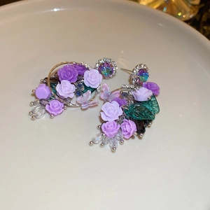 Détail de boucles d'oreilles fleurs en acrylique violettes et feuilles vertes sur plat