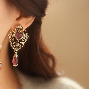 Close-up of vintage gold earring with purple heart crystal worn by a model