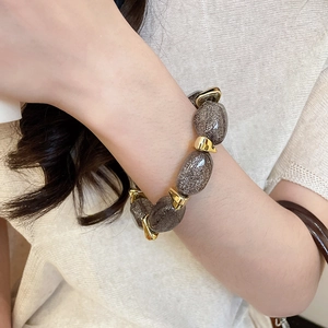 Close-up of dark grey oval acrylic beads with gold irregular spacers on a wrist
