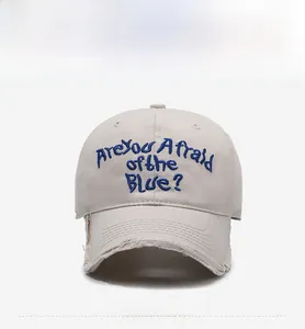Detail view of beige baseball cap with blue embroidery and distressed vintage edges