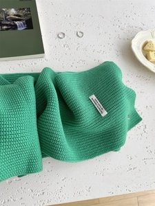 Dettaglio di sciarpa in maglia di lana verde con etichetta su marmo bianco