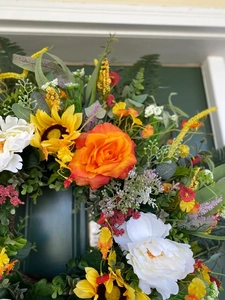 Close-up of artificial summer wreath with orange roses, sunflowers and mixed greenery