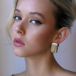 Boucles d'oreilles rectangulaires dorées avec motif ondulé portées par un mannequin