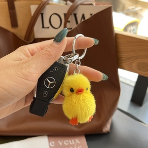 Mini plush yellow duck keychain with soft fur detail hanging next to luxury car keys