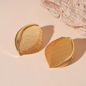 Close-up of golden abstract leaf textured earrings on a minimalist beige stone background