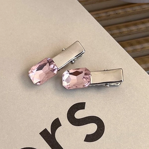 Close-up of pink crystal heart hair clips with silver metal base on textured card
