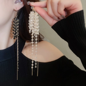 Dettaglio di orecchini a nappina in oro con perle di vetro nere e trasparenti su modella