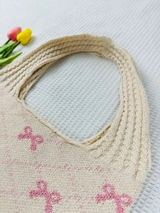 Close-up of cream knit tote bag with pink bow patterns and thick woven handle texture