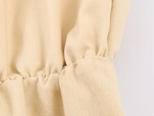 Detail of smocked elastic cuff and woven texture on beige long sleeve dress