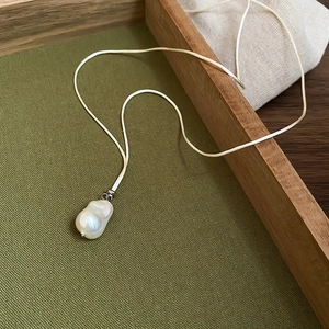 Detail of baroque pearl pendant with iridescent luster on green textured fabric