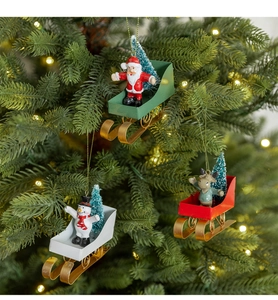 Close-up of Santa, snowman, and reindeer metal sled ornaments hanging on a Christmas tree