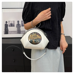 Detail of white shell bag with metallic ring handle and embossed elephant artwork