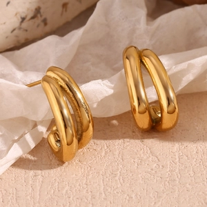 Macro detail of 18K gold plated double hoop earrings on a textured beige background