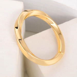 Detailed close-up of a modern twisted gold ring with a polished mirror finish on white block