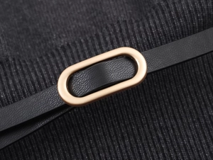 Détail d'une robe en tricot noir avec une ceinture en cuir et une boucle ovale dorée