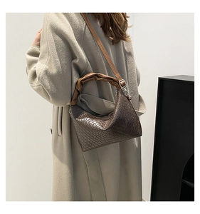 Detail of dark brown crescent bag featuring crocodile texture and pleated handle strap