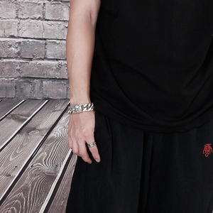 Detail view of men's stainless steel Cuban link bracelet with skull charms on wrist