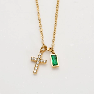 Detail of gold-plated cross necklace with emerald green gemstone and white zircon stones