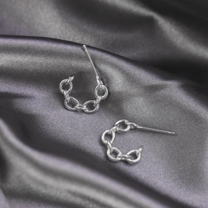 Detail shot of silver link chain earrings on a luxurious grey silk fabric background