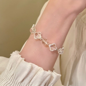 Detailed close-up of a silver four-leaf clover bracelet with clear crystal beads on a wrist