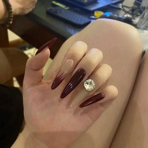 Long pointed press-on nails in burgundy and nude gradient with a large diamond rhinestone