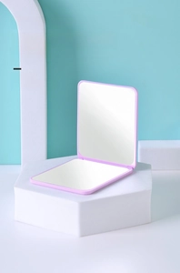 Detail of portable double-sided folding makeup mirror in purple on a minimalist display