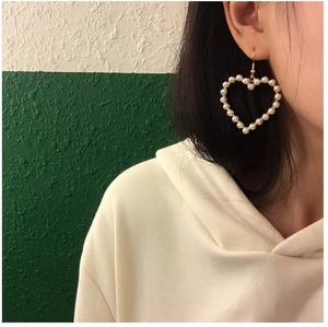 Detail view of large heart-shaped pearl drop earrings on a model showing actual scale