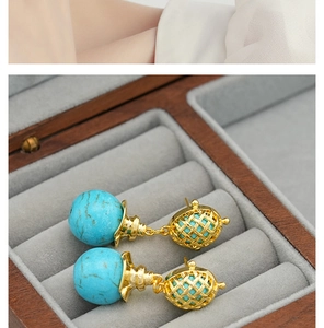 Detail of turquoise drop earrings with hollow gold metal weaving balls in a wooden box