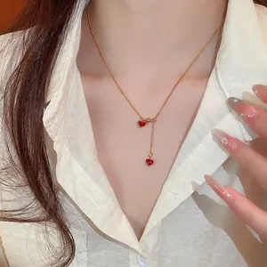 Gold chain necklace with double red enamel heart pendants worn on neck by a model