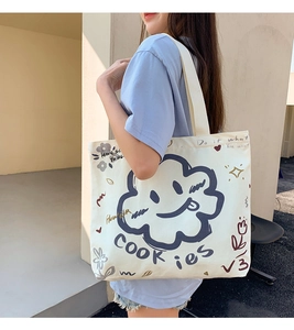 Detail showing off-white canvas tote bag with navy blue cartoon cloud and text prints