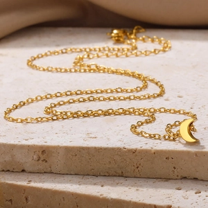 Polished gold crescent moon pendant on fine chain over natural stone surface