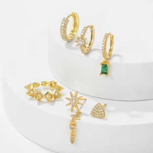 Golden geometric tassel earrings set with green zircon stones on a white stand