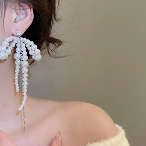 Detail of silver bow tassel pearl earrings worn by model for an elegant look