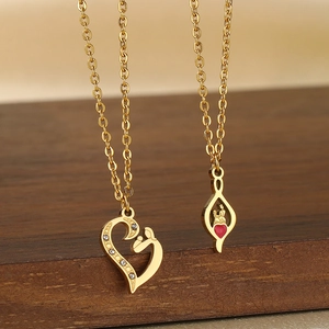 Détail de deux colliers en titane doré avec pendentifs cœur en diamant et émail rouge